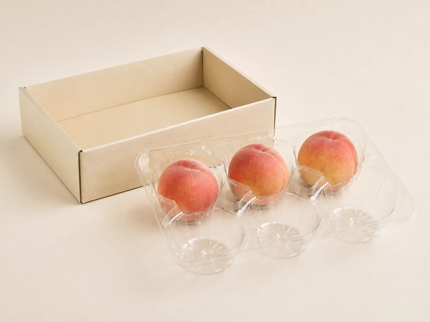 AI packaging illustration: a transparent six-pocket peach support tray with three peaches still seated and three empty visible wells, lifted out of a plain cream gift carton resting beside it