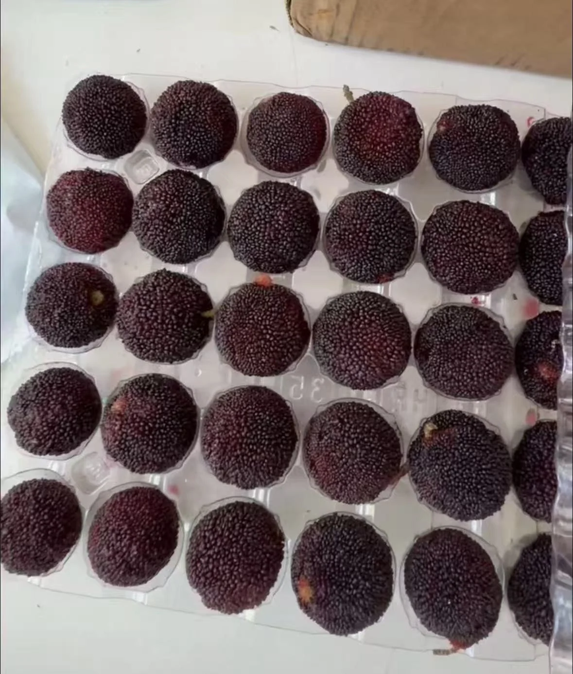 These Chinese bayberries show pressure, rubbing, and juice even though the two-piece package remains intact. Inspect the fruit, not only the container.
